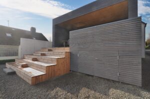 Holzhaus mit dunkler Fassade, Holzterrasse und Außentreppe