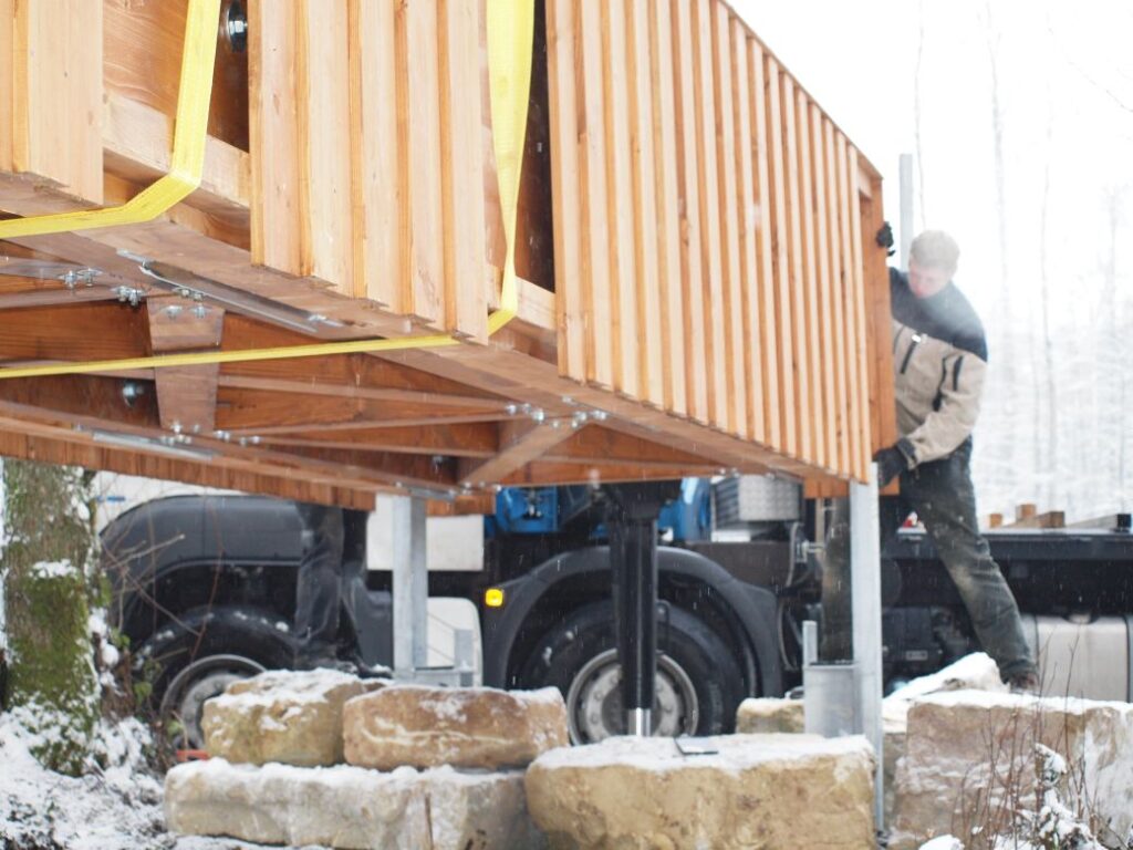Holzbrücke wird per Kran auf Steinfundamente gesetzt