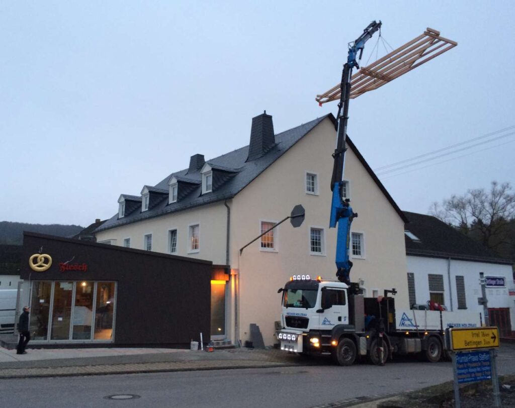 Ein Kran hebt ein vorgefertigtes Holzelement auf den Anbau einer Bäckerei