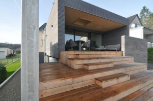 Dunkel verkleidetes Holzhaus mit überdachter Terrasse und breiten Holzstufen