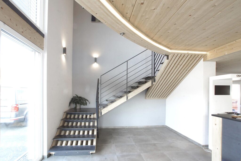 Innenraum mit Treppe, geschwungener Holzdecke und großer Fensterfront