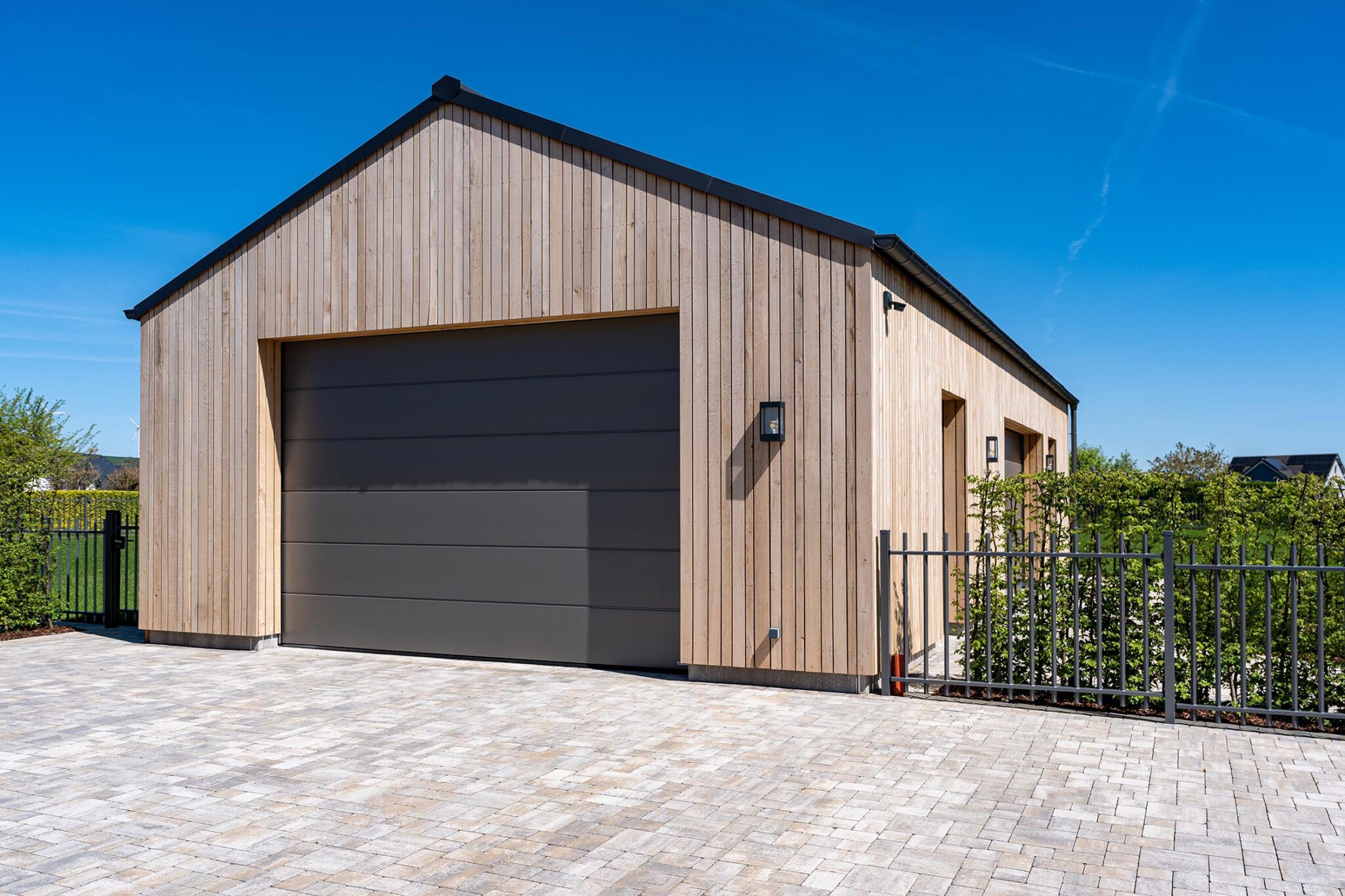 Garage in Holzrahmenbau mit vertikaler Holzfassade und grauem Garagentor