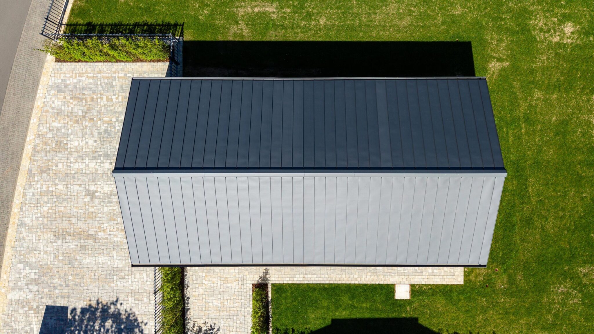 Luftaufnahme eines Flachdachgebäudes mit Holzfassade neben einem Wohnhaus