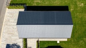 Luftaufnahme eines Flachdachgebäudes mit Holzfassade neben einem Wohnhaus