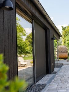 Detail einer dunklen Holzfassade mit Blick in den Garten