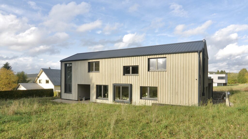 Zweigeschossiges Holzhaus mit vertikaler Lärchenfassade und Satteldach auf einer Wiese