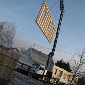 Un pont roulant remonte un élément mural préfabriqué en bois jusqu'au chantier.