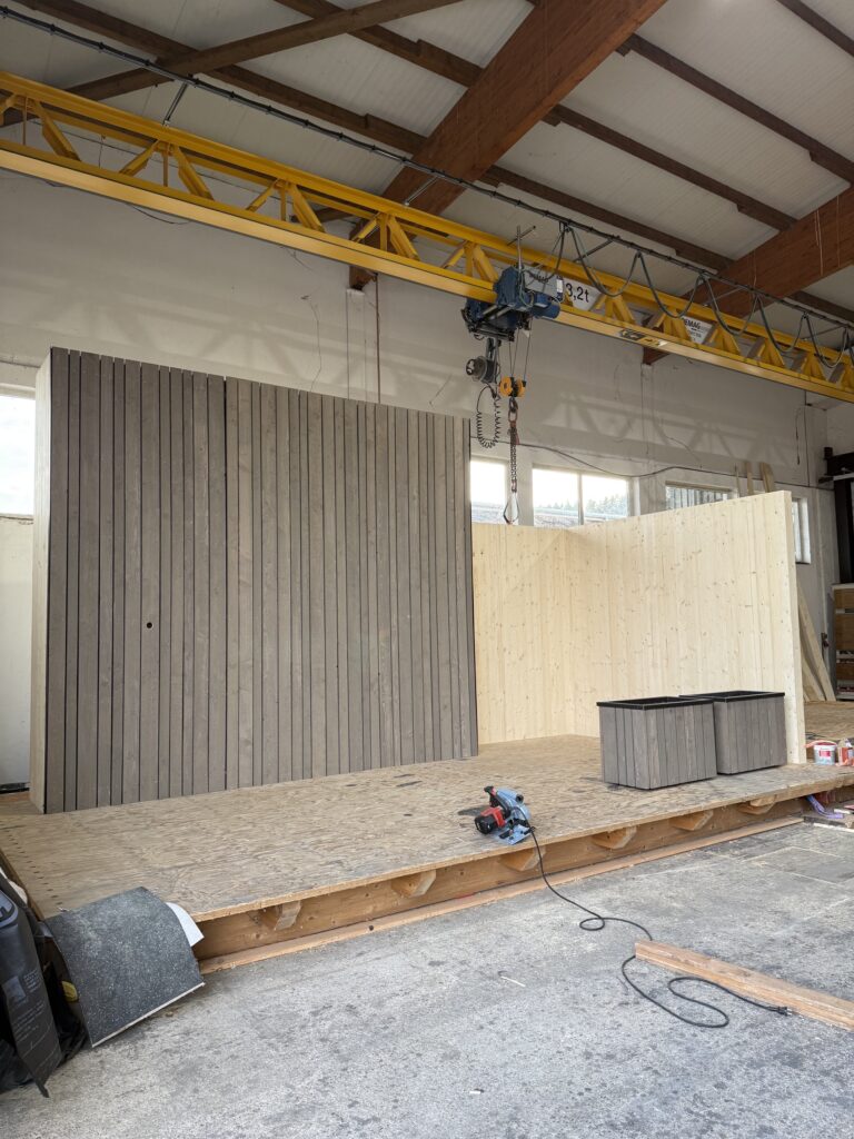 Holzverkleidete Rückwand und helle Sitznische des Messestands in der Werkstatt