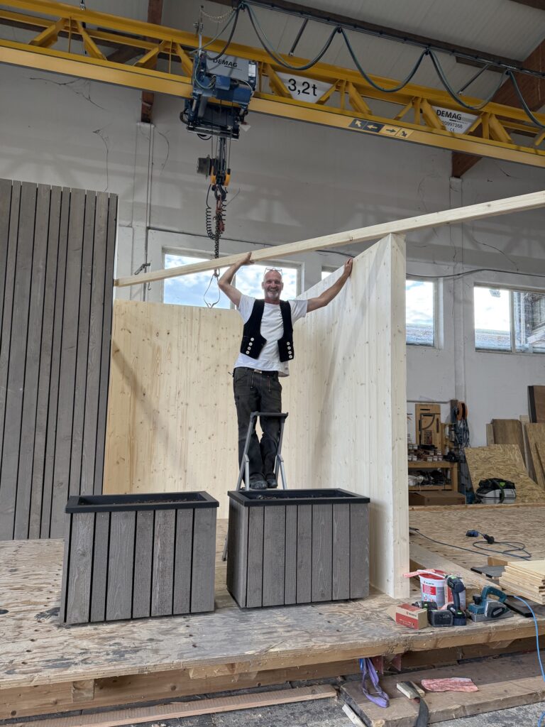 Aufbau des Messestands in der Werkstatt: Ein Balken wird über Kopf gehalten
