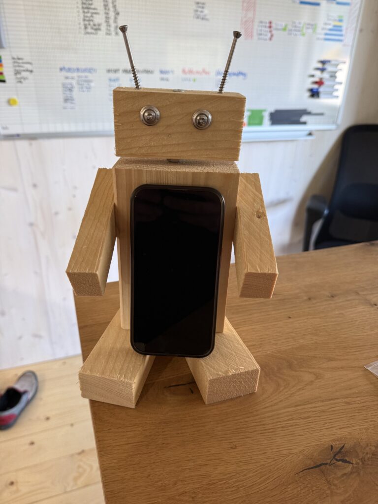 Der Holzbot als Handyhalter: Zwischen seinen Füßen steht ein Smartphone