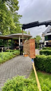 Leimholzträger schwebt am Kran über den Parkweg